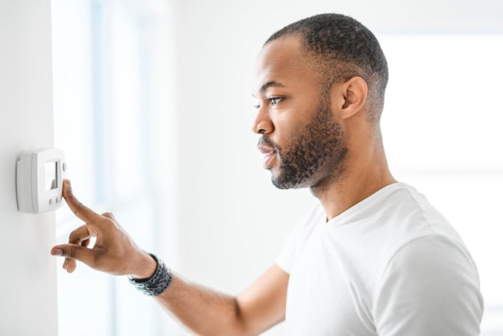 A man adjusts a digital thermostat on a white wall to control the temperature in his home.