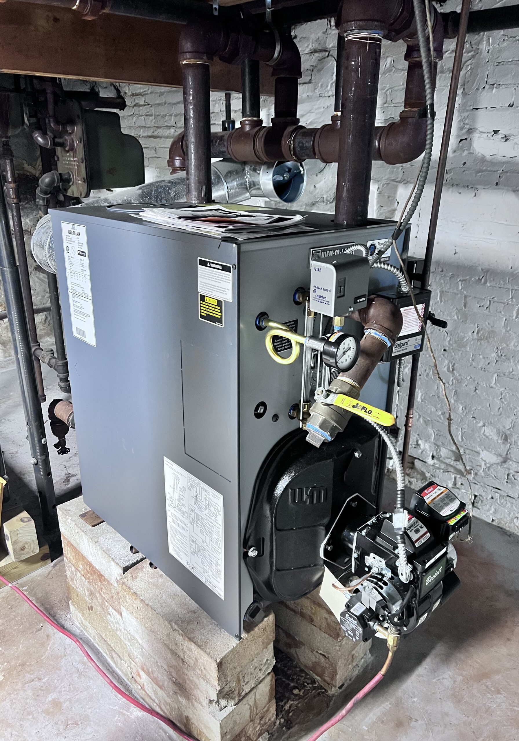 boiler 2 High-efficiency stainless steel boiler installed on a concrete base in a residential setting, with visible plumbing connections and pressure gauge, emphasizing optimal heating solutions for homes and businesses.